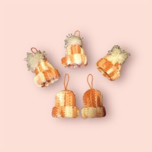 Five Pink Winter Hat Ornaments, featuring knitted orange and cream stripes with small fluffy pom-poms on top, are arranged on a light pink background. Perfect for adding a festive touch, each hat includes a loop for hanging as charming Christmas decorations.