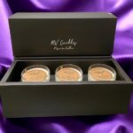 A black and gold presentation box containing 3 candles